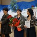 Zdjęcie przedstawia trzy Panie z KGW z Bucza. Jedna z nich trzyma promesę, którą otrzymały z okazji 20-lecia działalności. Pani pośrodku natomiast trzyma kwiaty. W tle ozdoby świąteczne.