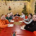Zdjęcie przedstawia grupkę dziewczyn siedzących przy dużym czerwonym stole i piszących do Świętego Mikołaja.