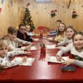 Zdjęcie przedstawia dzieci siedzące przy dużym czerwonym stole i piszą list do Świętego Mikołaja.
