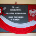 Zdjęcie prezentuje tablicę korkową, na której widnieje napis "20-lecie nadania imienia Powstańców Wielkopolskich Szkole Podstawowej w Przemęcie. Tablice zdobi też flaga Polski, flaga Powstania Wielkopolskiego oraz duże kwiaty z papieru w barwach Polski.