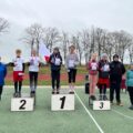 Na zdjęciu uczniowie na podium z dyplomami i medalami. Koło nich stoją nauczyciele.