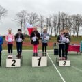 Na zdjęciu uczniowie na podium z dyplomami i medalami. Koło nich stoją nauczyciele.