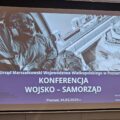 Na zdjęciu widoczna grafika wyświetlana na projektorze. Na grafice widnieje temat konferencji.