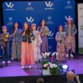 Na zdjęciu widzimy grupę dzieci występujących na scenie podczas wydarzenia. Dziewczynki ubrane są w kwiatowe sukienki, a chłopcy w koszule. Wszyscy trzymają mikrofony i śpiewają. W tle znajdują się ścianki i roll up, na których widnieją logotypy związane z Samorządem Województwa Wielkopolskiego oraz hasło "Wielkopolska Odnowa".