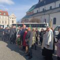 Na zdjęciu delegacje sołtysów z różnych gmin stoją na dworze przed pomnikiem św. Jana Pawła II.