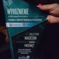 Na zdjęciu widoczna jest statuetka, która stanowi wyróżnienie w wojewódzkim konkursie „Fundusz Sołecki Najlepsza Inicjatywa”. Statuetka ma nowoczesny, trójkątny kształt, wykonana jest z przezroczystego szkła w odcieniach niebieskiego. Na jej powierzchni widnieje napis: „WYRÓŻNIENIE” dla sołectwa Kaszczor (gmina Przemęt). Na dole statuetki znajduje się napis: „Krzysztof Grabowski, Wicemarszałek Województwa Wielkopolskiego" oraz logo „Wielkopolska Odnowa Wsi” i data „2025”.