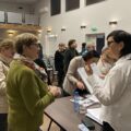 Na zdjęciu widać panią z ZUS, która tłumaczy coś kobiecie przybyłej na spotkanie. W tle znajdują się inni uczestnicy spotkania.