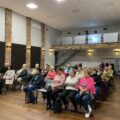 Na zdjęciu widać uczestników spotkania siedzących na krzesłach.