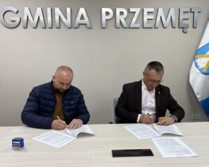 Na fotografii wójt i pan Sławomir podpisują umowę. W tle srebrny napis "Gmina Przemęt"