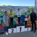 Na zdjęciu trójka dzieci stojących na podium z medalami i pucharami. Na fotografii obecni są także wójt gminy oraz dyrektor szkoły.