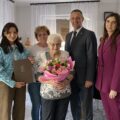 Na fotografii wójt, pracownik USC pani Natalia oraz jubilatka wraz z osobami z rodziny. Jubilatka pozuje z bukietem kwiatów.
