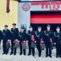 Na fotografii strażacy ustawieni w rzędzie. W rękach trzymają upominki.