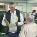 Na fotografii mężczyzna, który pokazuje dziennikarce dwie odmiany szparagów: białe i zielone.