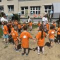 Na zdjęciu widoczne są dzieci, które wraz z nauczycielkami stoją, tworząc duże kółko.