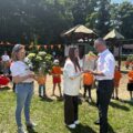 Na zdjęciu uchwycono moment wręczenia grawertonu wójtowi przez dyrektorkę. Na zdjęciu widoczna także nauczycielka, która trzyma kwiatka w doniczce.