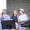Na zdjęciu widoczne trzy dziewczyny na scenie podczas śpiewania piosenki.