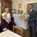 Na fotografii wójt składa życzenia i wręcza jubilatce bukiet kwiatów.