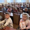 Na zdjęciu widoczni przedszkolacy siedzący w sali sesyjnej w urzędzie. Niektórzy z nich trzymają laurki.