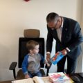 Na zdjęciu widoczny chłopiec, który siedzi na fotelu wójta. Wójt trzyma w dłoni otrzymaną od chłopca laurkę.
