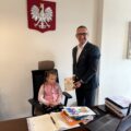 Na zdjęciu widoczna dziewczynka, która siedzi na fotelu wójta. Wójt trzyma w dłoni otrzymaną od niej laurkę.