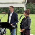 Na zdjęciu kobieta i mężczyzna. Kobieta śpiewa, a mężczyzna przygrywa jej na keyboardzie.