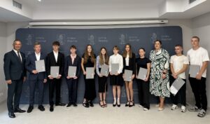 Grupowe zdjęcie nagrodzonych uczniów wraz z wójtem i kierownikiem wydziału oświaty. Wszyscy pozują na tle dużej granatowej ścianki z herbem gminy Przemęt.