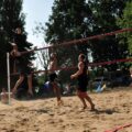 Na zdjęciu zawodnicy wykonują dynamiczną akcję podczas meczu. Jeden z graczy skacze, starając się zablokować piłkę, podczas gdy drugi przygotowuje się do ataku.
