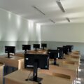 Widzimy klasę komputerową, w której znajdują się biurka z monitorami i krzesłami.