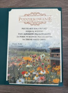 Na zdjęciu znajdują się podziękowania w formie listu. Główny tytuł na górze to „PODZIĘKOWANIE”. Dokument wyraża wdzięczność pszczelarzy z „Koła Przemęt” dla pana Janusza Frąckowiaka za pomoc w rozwoju pszczelarstwa na terenie gminy. Certyfikat podpisany jest przez prezesa Koła, Piotra Lehmanna. Na dole na środku strony znajduje się informacja o miejscu i roku: „Przemęt 2025r.” Projekt dokumentu zawiera tło z obrazem kwiecistej łąki, na której latają pszczoły, a obok widoczna jest pasieka, co nawiązuje do tematyki pszczelarstwa.