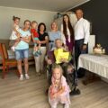 Wspólne zdjęcie, na którym znajduje się wójt, pracownik urzędu oraz jubilatka wraz ze swoimi bliskimi. Jubilatka trzyma bukiet kwiatów i list gratulacyjny.