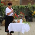 Na fotografii sołtys Kaszczoru Beata Binkowska, która wygłasza przemówienie, ubrana w strój ludowy. Przed nią stoi stół z dekoracjami, w tym bukietem kwiatów i chlebem.
