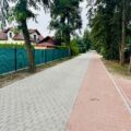 Na zdjęciu przedstawiono fragment wyremontowanej ulicy Starkowskiej. Po lewej stronie widoczne są ogrodzenia posesji, a po prawej drzewa. Jej główną, szarą część wykonano z kostki ażurowej, a obok niej przebiega czerwony pas z kostki brukowej, przeznaczony dla pieszych i rowerzystów.