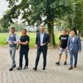Na fotografii widać grupę osób uczestniczących w odbiorze inwestycji, idą wzdłuż nowo wybudowanej drogi i rozmawiają. Po obu stronach trasy rosną rzędy drzew.