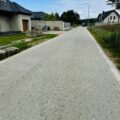 Na fotografii widoczna jest nowa droga, wykonana z kostki brukowej. Po obu stronach ulicy znajdują się domy.