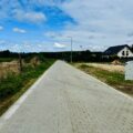 Na fotografii widoczna jest nowa droga, wykonana z kostki brukowej. W oddali widać domy.