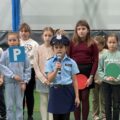 Na zdjęciu widoczna dziewczynka przebrana za policjantkę podczas występu artystycznego. W tle inni uczniowie.