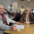Na zdjęciu dwóch uczestników turnieju, którzy siedzą przy stoliku. W tle inni uczestnicy.