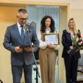Na zdjęciu wójt, który odczytuje życzenia z listu gratulacyjnego dla seniorów podczas uroczystości. Obok wójta dyrektor GCKiB Agnieszka Klugiewicz, która trzyma promesę oraz zastępca dyrektora GCKiB, która trzyma bukiet kwiatów.