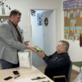 Na zdjęciu widoczny pan Łukasz, który rozdaje odblaskowe kamizelki seniorom.