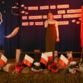 Na zdjęciu widoczna dziewczyna podczas występu na scenie. Scena udekorowana jest w narodowe barwy.
