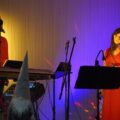 Na zdjęciu widoczna kobieta i mężczyzna podczas występu na scenie. Kobieta śpiewa, a mężczyzna gra na keyboardzie.