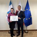 Na fotografii wójt wraz z sołtysem Borku pozują z czekiem. W tle widoczne są flagi: Polski, Unii Europejskiej oraz z herbem gminy Przemęt.