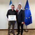 Na fotografii wójt wraz z sołtysem Górska pozują z czekiem. W tle widoczne są flagi: Polski, Unii Europejskiej oraz z herbem gminy Przemęt.