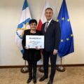 Na fotografii wójt wraz z sołtysem Kaszczoru pozują z czekiem. W tle widoczne są flagi: Polski, Unii Europejskiej oraz z herbem gminy Przemęt.
