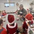 Na zdjęciu widoczna kobieta, która lukruje pierniczki, a dzieci się temu przyglądają.