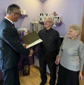 Na fotografii widoczny wójt, który odczytuje życzenia z listu gratulacyjnego jubilatowi. Na zdjęciu widoczna także małżonka jubilata.