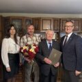 Na zdjęciu wójt Janusz Frąckowiak, pracownik USC Natalia Chomska oraz jubilat wraz z synem. Jubilat pozuje z listem gratulacyjnym.