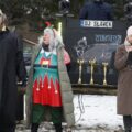 Na zdjęciu widoczna kobieta, która przemawia przez mikrofon. Koło niej stoją organizatorzy wydarzenia.