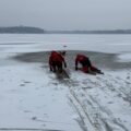 Na fotografii strażacy w specjalistycznym sprzęcie prowadzą pokazową akcję ratunkową na zamarzniętym jeziorze. Ratownicy poruszają się po lodzie przy użyciu sprzętu asekuracyjnego i lin, demonstrując sposób udzielania pomocy osobie pod którą załamał się lód.