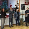 Na fotografii widoczny jest wójt, który przemawia podczas wydarzenia. Koło niego stoją organizatorzy wydarzenia oraz kierownik wydziału oświaty z gminy.